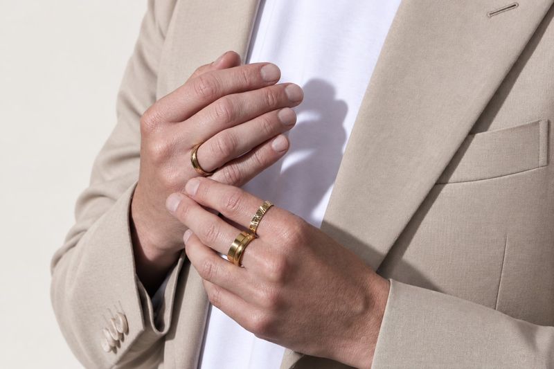 mains d'un homme en costume beige portant plusieurs alliances en or jaune
