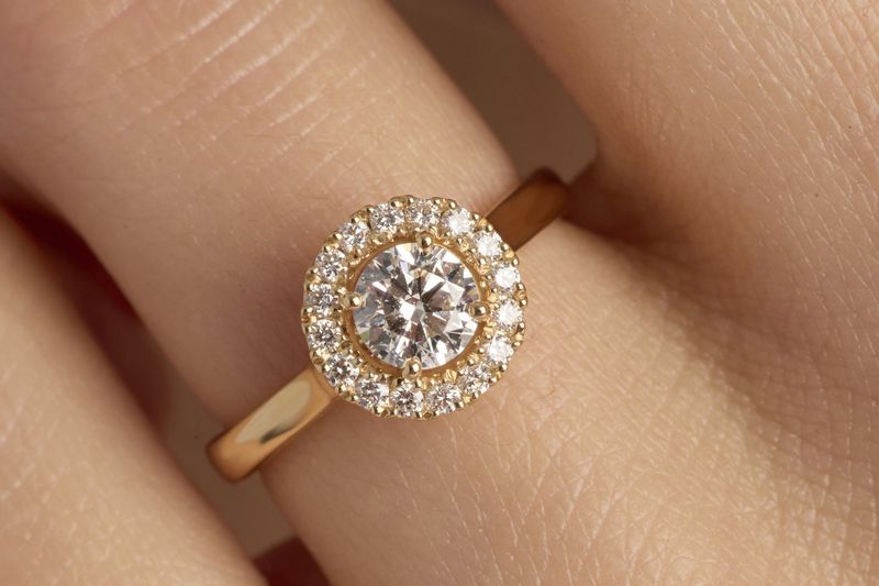 solitaire halo de diamants en or jaune porté au doigt